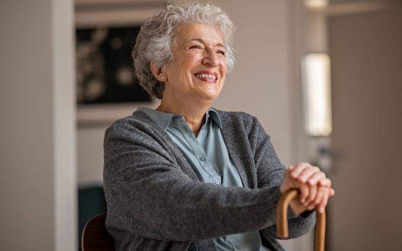 elderly woman with a cane, sits in a room and smiles