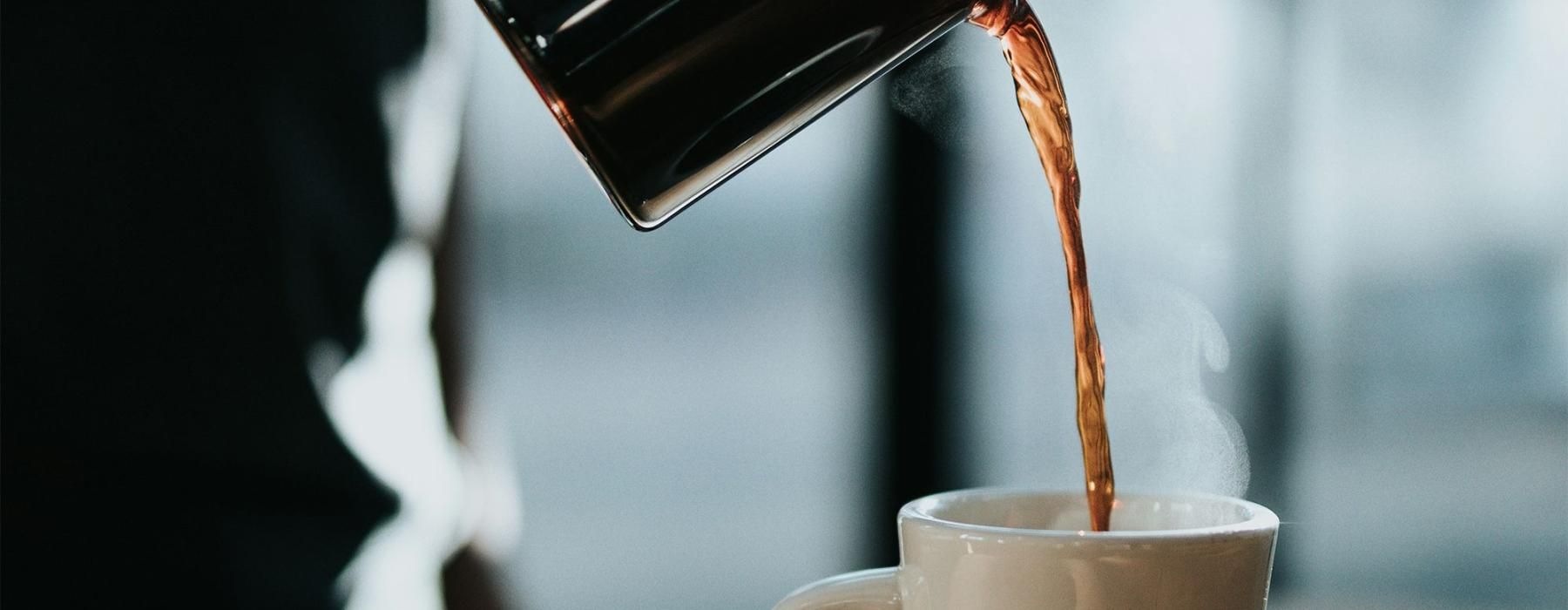 a person pouring a carafe of coffee into a cup